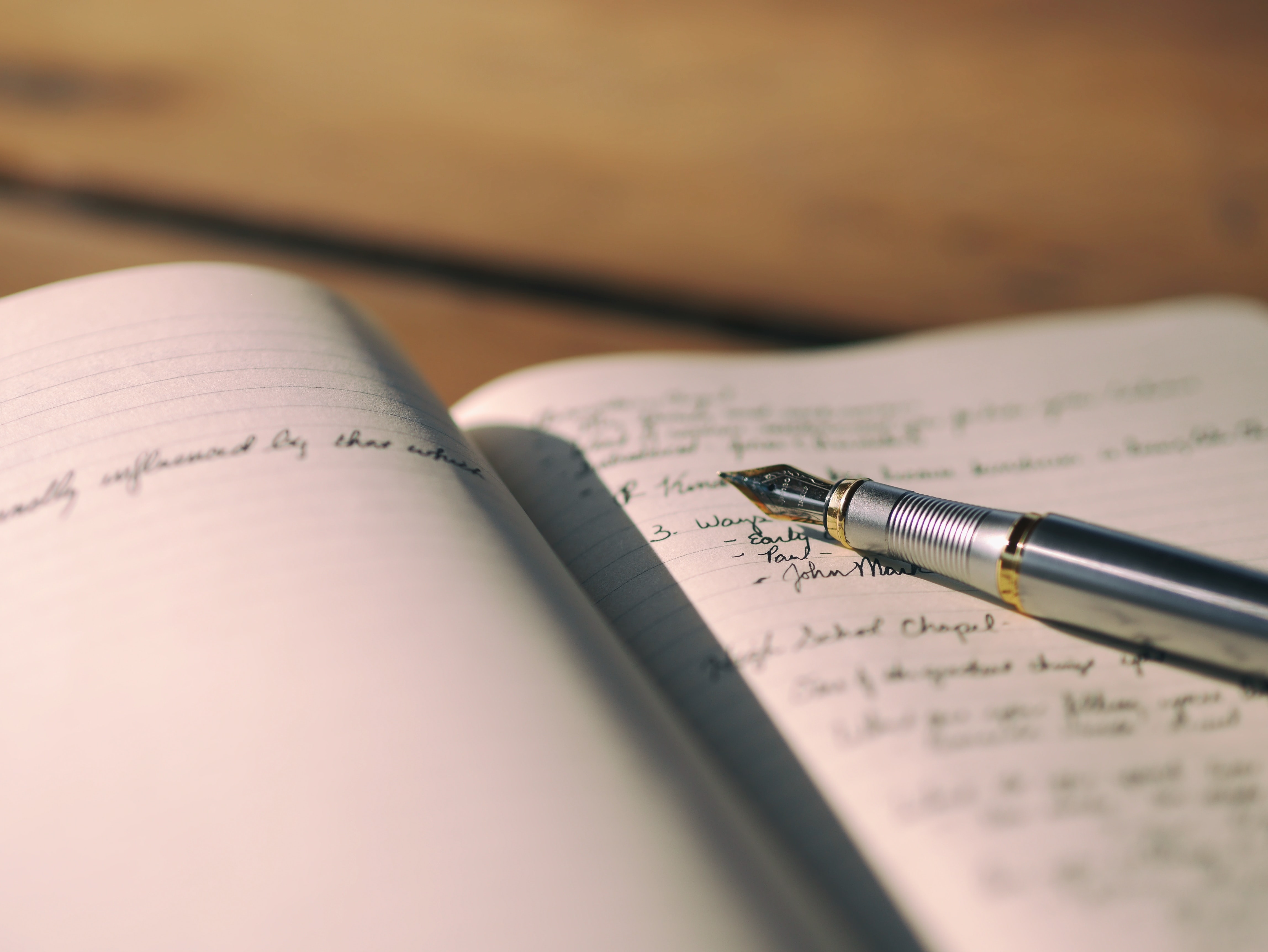 A journal lies open, handwriting visible on the right side of a page beneath a fountain pen.