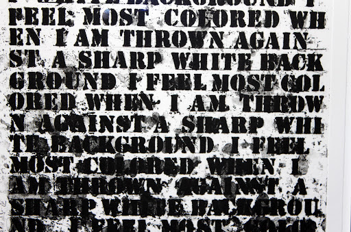 A detail from Glenn Ligon's Untitled (I Feel Most Colored...) (1992), a text-based work that features the phrase "I feel most colored when I am thrown against a sharp white background" screen-printed multiple times over a canvas. As the text repeats, the ink becomes heavier, blacking out the page until the text becomes illegible.