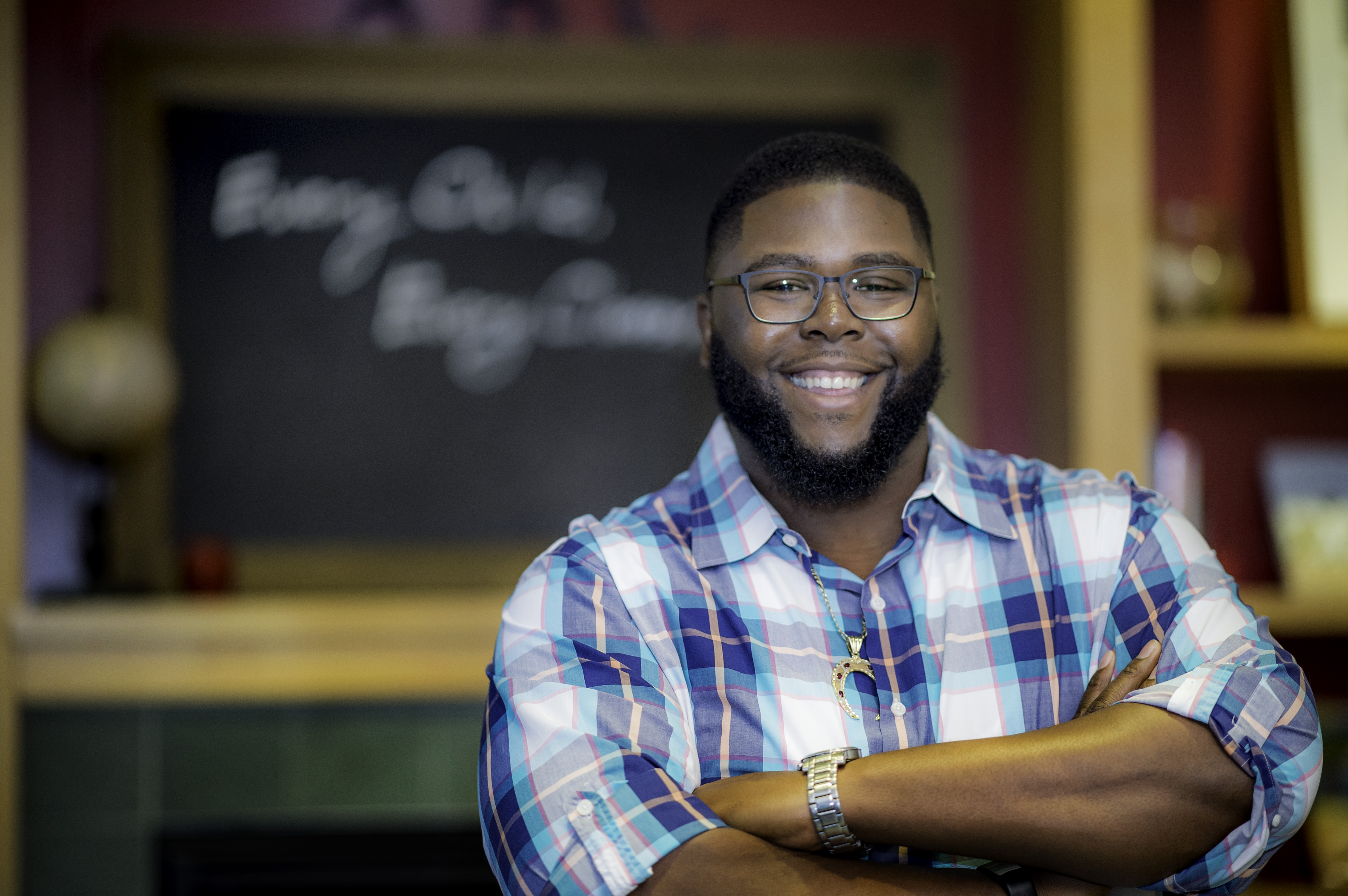 Anthony Jack smiles with crossed arms in front of an out-of-focus chalkboard.