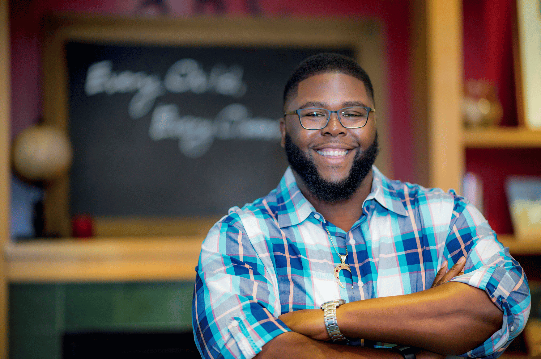 Anthony Jack smiles with crossed arms in front of an out-of-focus chalkboard.