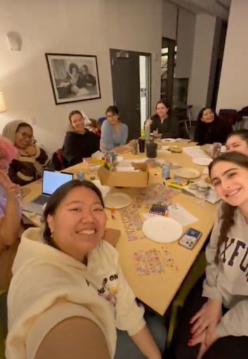 A facilitator takes a selfie with participants seated around the table, smiling and posing for the picture. The facilitator is at the bottom left corner holding up their phone and smiling, while another to their left holds up a peace sign. 