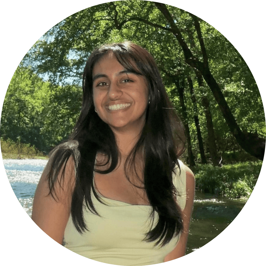 Divya is standing outside and wears a yellow top.