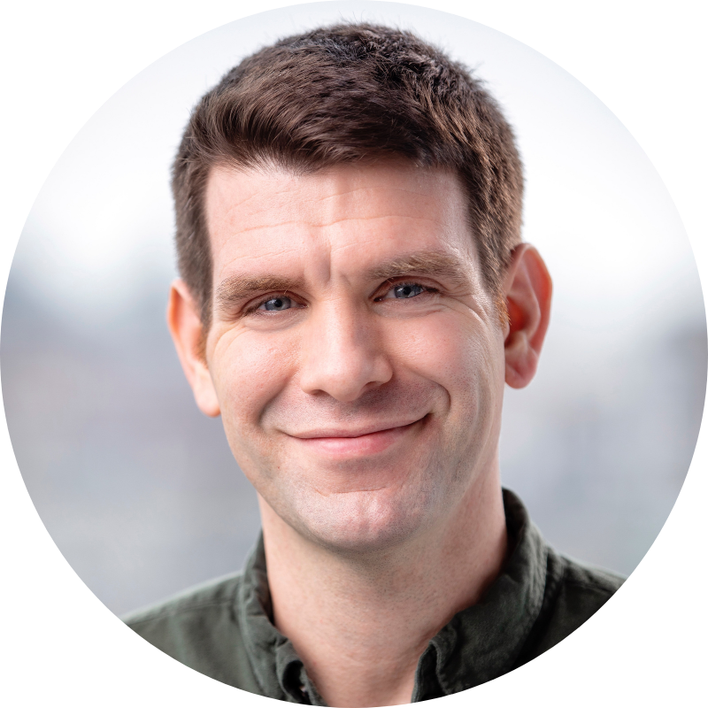 Nicholas Bartlett wears a green collared shirt and smiles at the camera with his mouth closed.