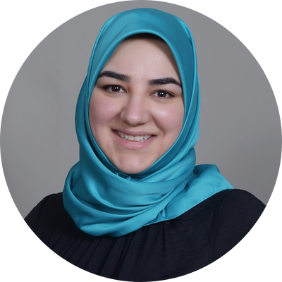Fatemeh Hosseini wears a black top and a deep sky blue hijab. She smiles at the camera with her mouth open in front of a solid gray background.
