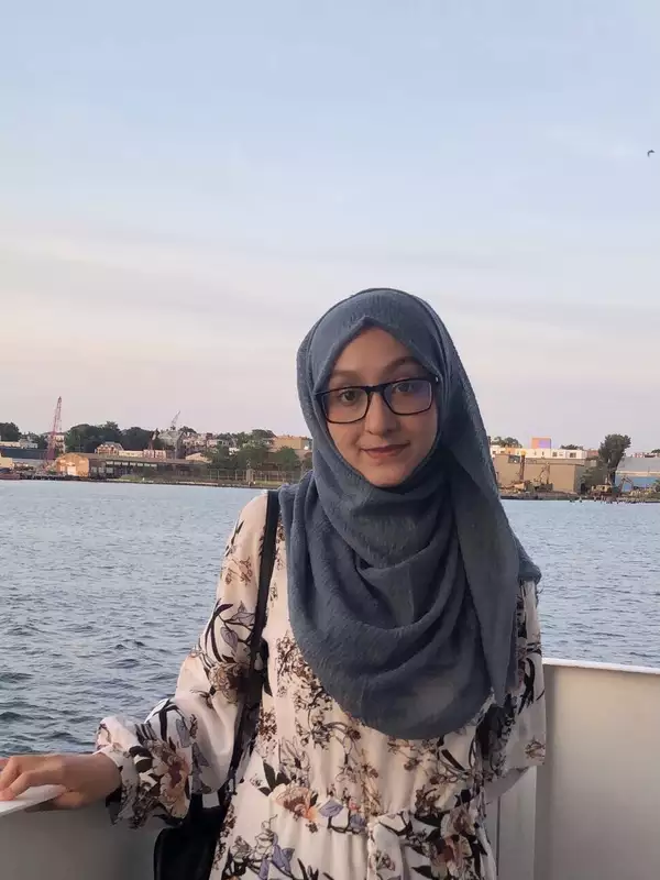 Sumayya Mokit standing in front of a waterfront, smiling at the camera.