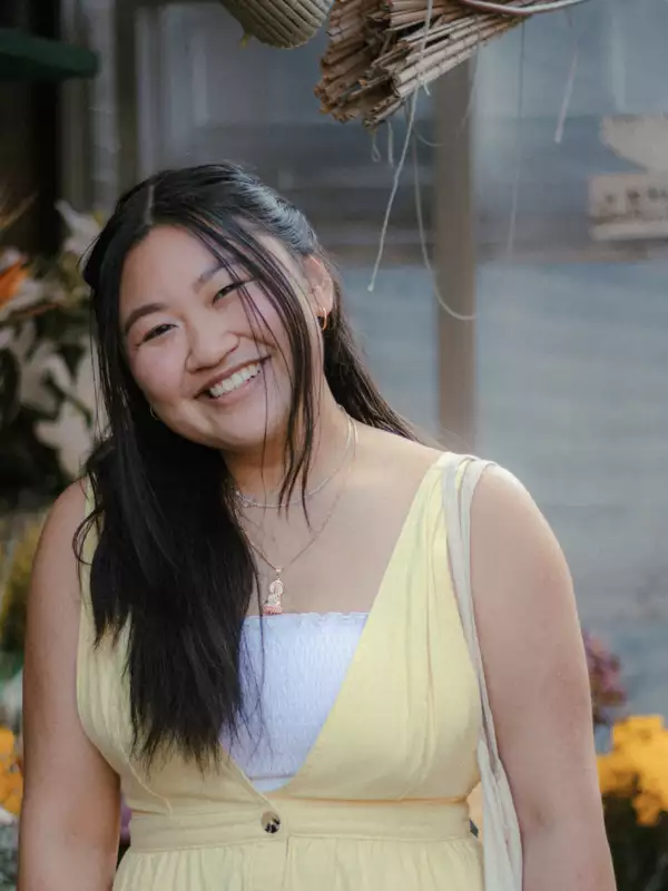 Tiffany in a yellow sleeveless top standing in front of floral decor.