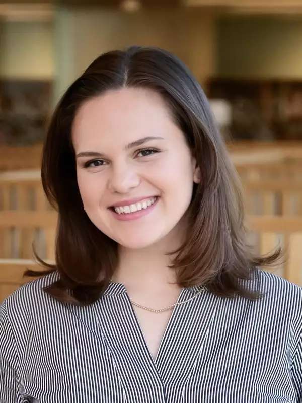 Alexa smiles at the camera while wearing a blue and white striped shirt. She is pictured inside the library.