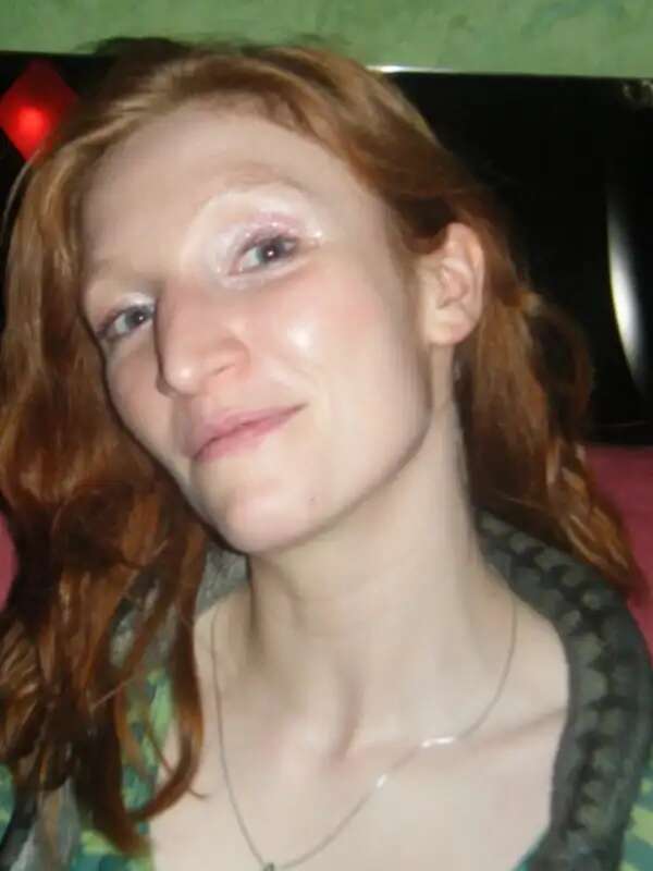 Charlotte is a white woman with red hair who tilts her head back and looks at the camera with a neutral expression. She is wearing a striped green shirt.